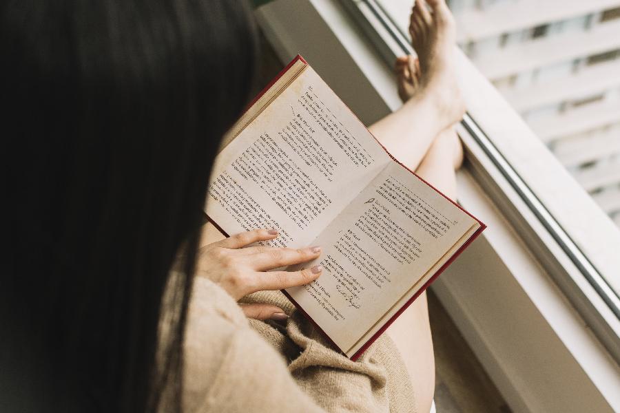 livros yoga Mulher lendo livro com os pés na janela - melhores livros sobre yoga